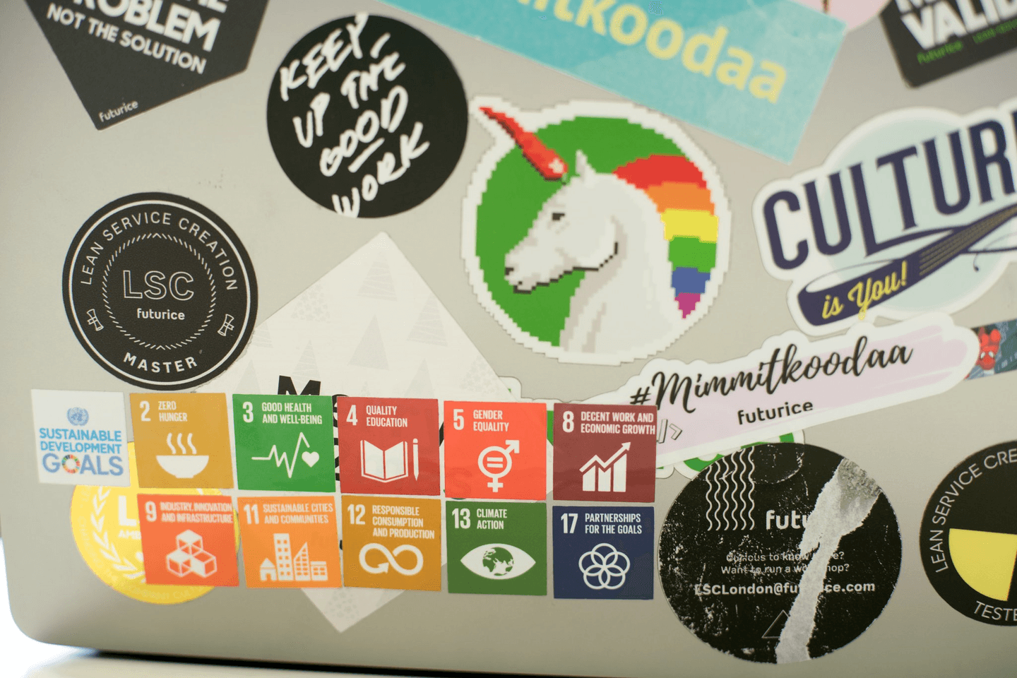 Collection of stickers on a surface including UN Sustainable Development Goals, a pixelated unicorn, and various motivational phrases.