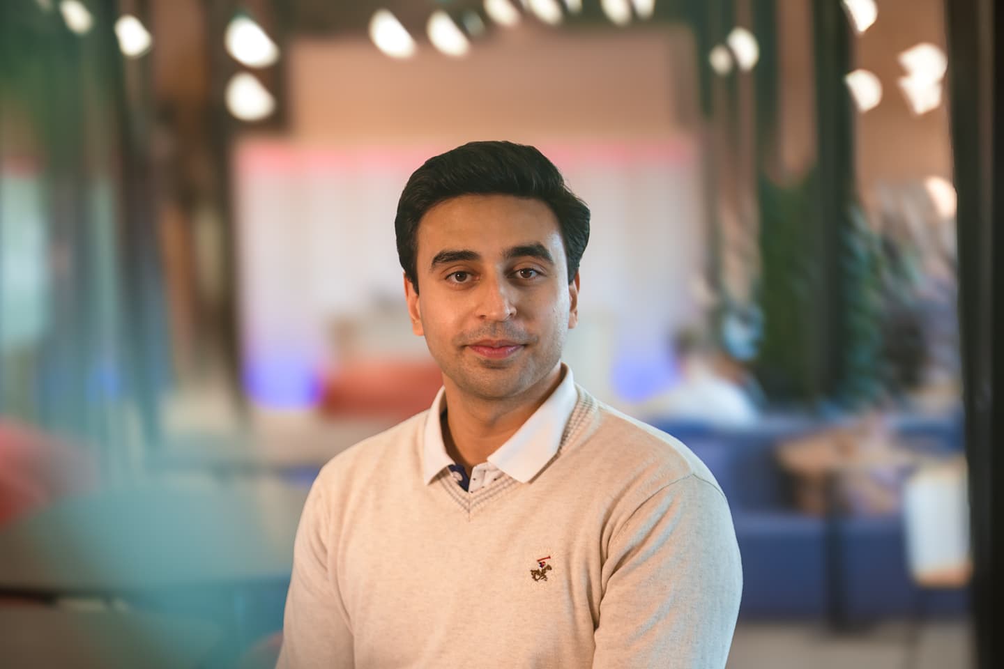 Person in light beige jumper with white collar in modern office space with blurred colourful background.